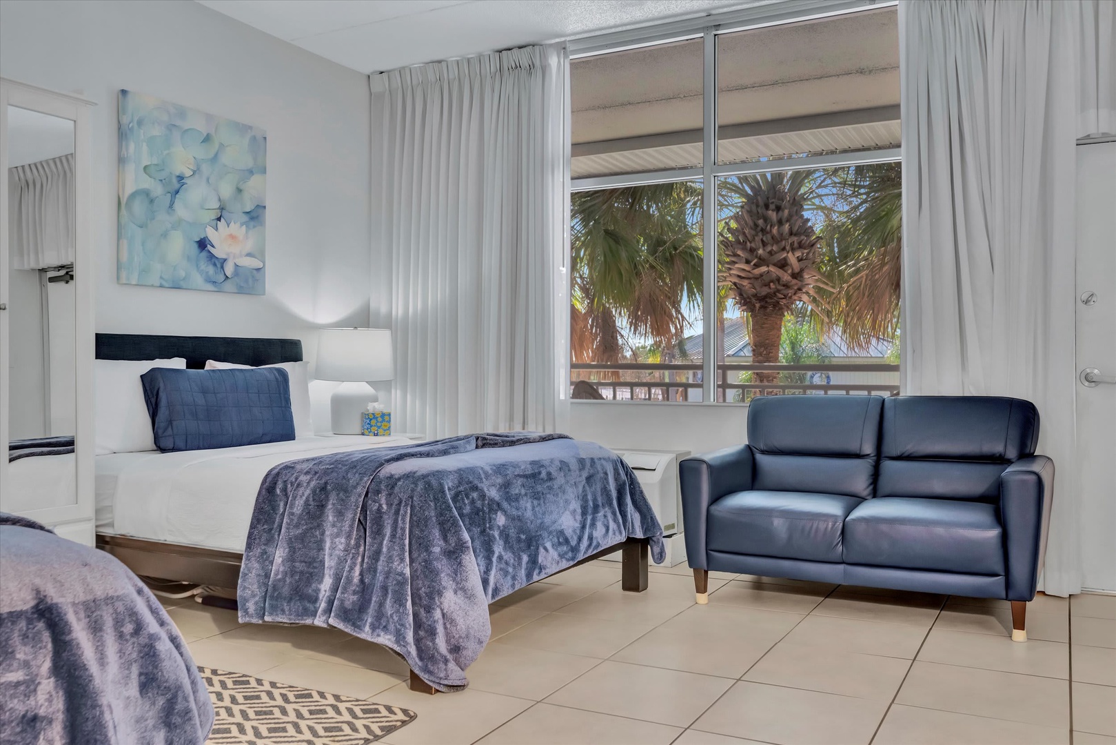 Unwind in your bright studio with two plush beds and a sleek loveseat. Through the window, palm trees sway just outside, setting a peaceful, tropical tone for your getaway.