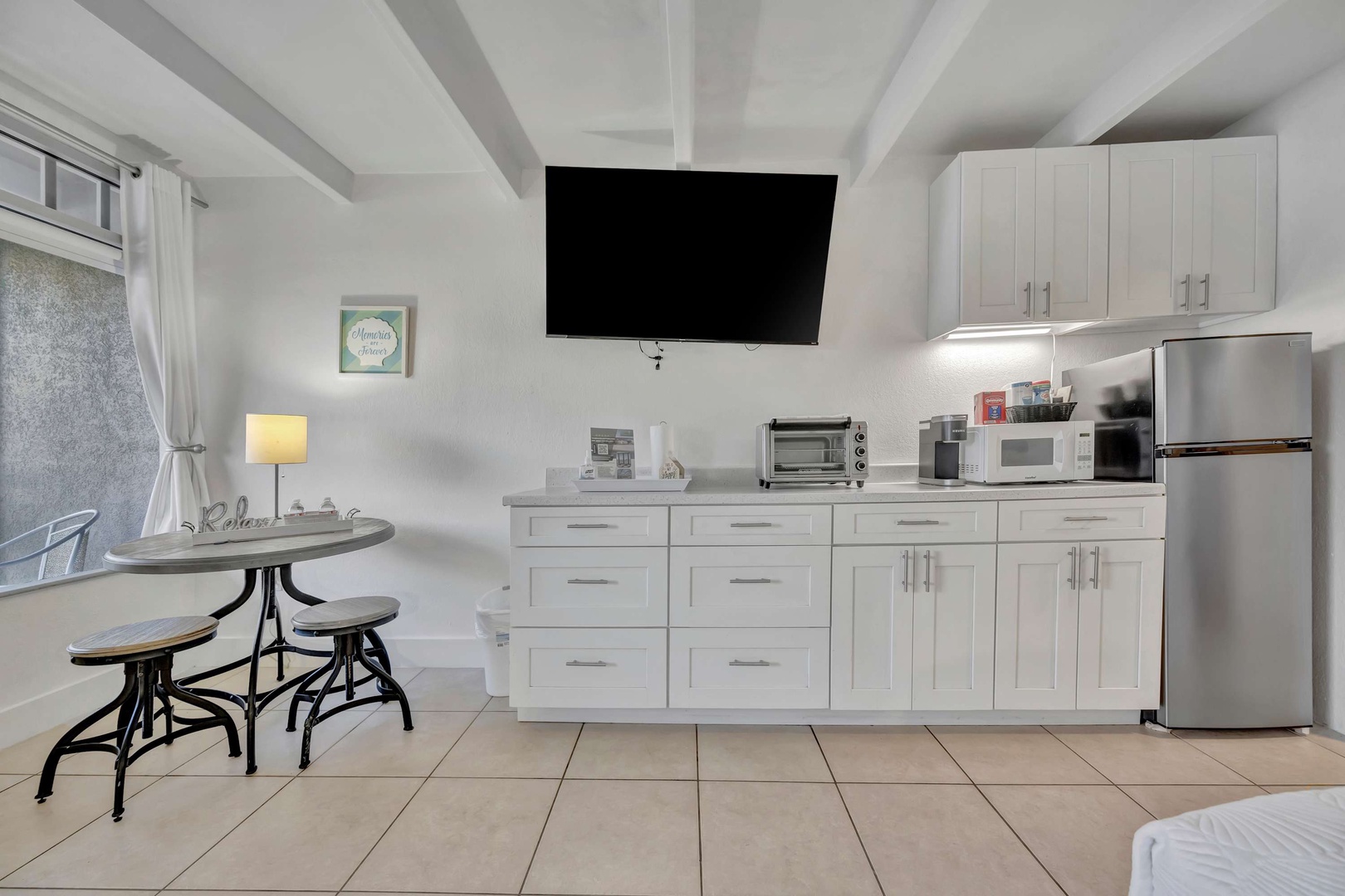 Your bright, open-concept studio features a full kitchen with modern appliances, a cozy dining nook by the window, and exposed beam ceilings that add character. Everything you need for a comfortable, convenient stay.