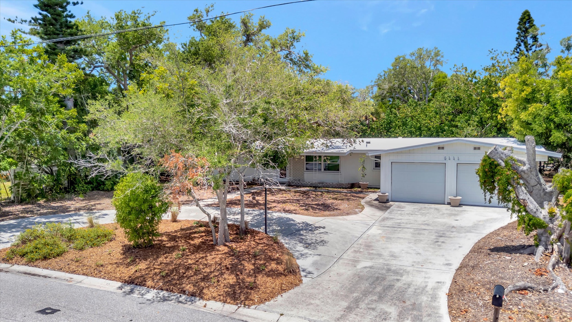 This single-story property sits on a tree-lined street with a spacious driveway and two-car garage. Lush greenery and mature trees surround the home, offering a peaceful, residential setting.