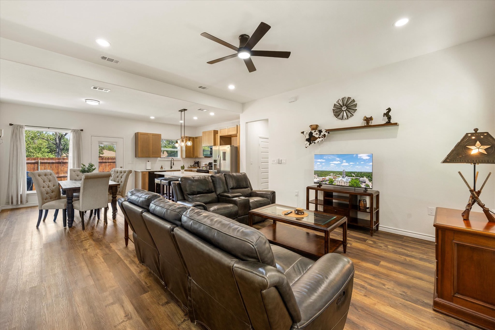 Open-plan living space with plush leather seating, warm wood floors, and fully equipped kitchen. Natural light floods the room while a modern ceiling fan keeps you comfortable.