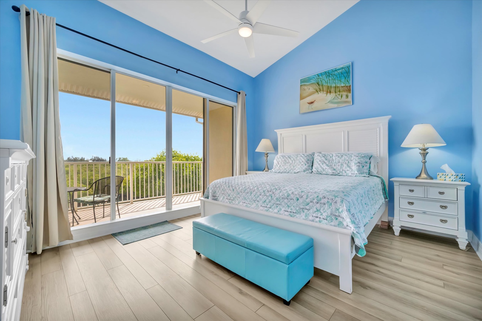 Wake up to natural light streaming through your balcony doors and serene views of lush greenery. This bright, beach-inspired bedroom offers coastal charm with soothing blue tones, crisp white furnishings, and plenty of space to unwind.