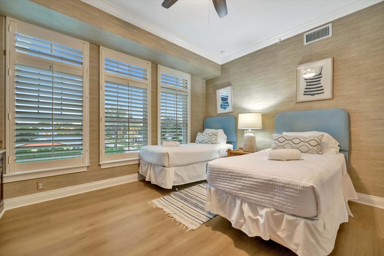 Your serene guest bedroom features two plush beds and soothing coastal tones, where natural light filters through plantation shutters and ceiling fans keep you comfortably cool.