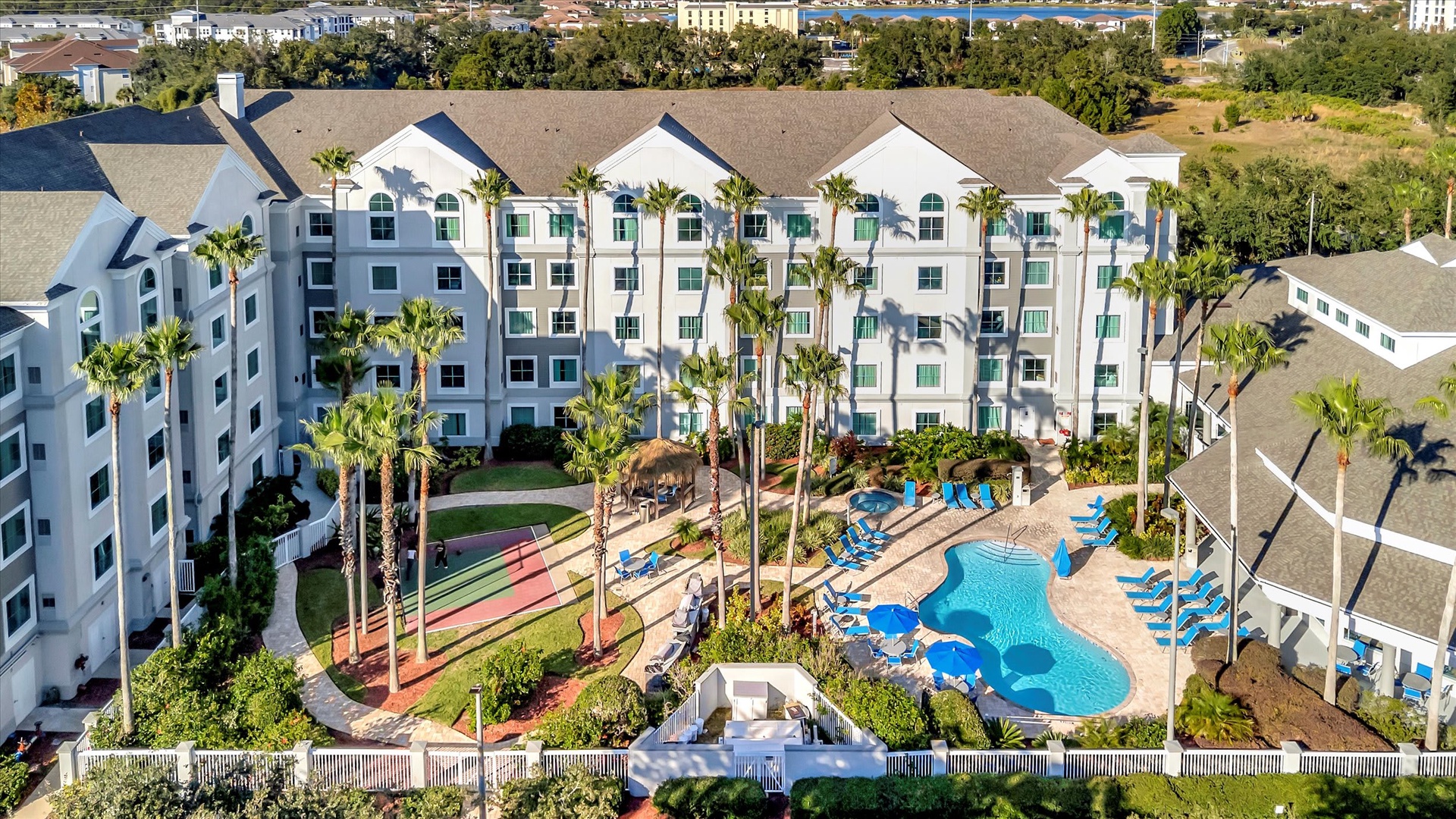 Aerial view of the resort property showcasing the multi-story buildings, tropical landscaping with palm trees, and a central pool area with loungers and recreational facilities.