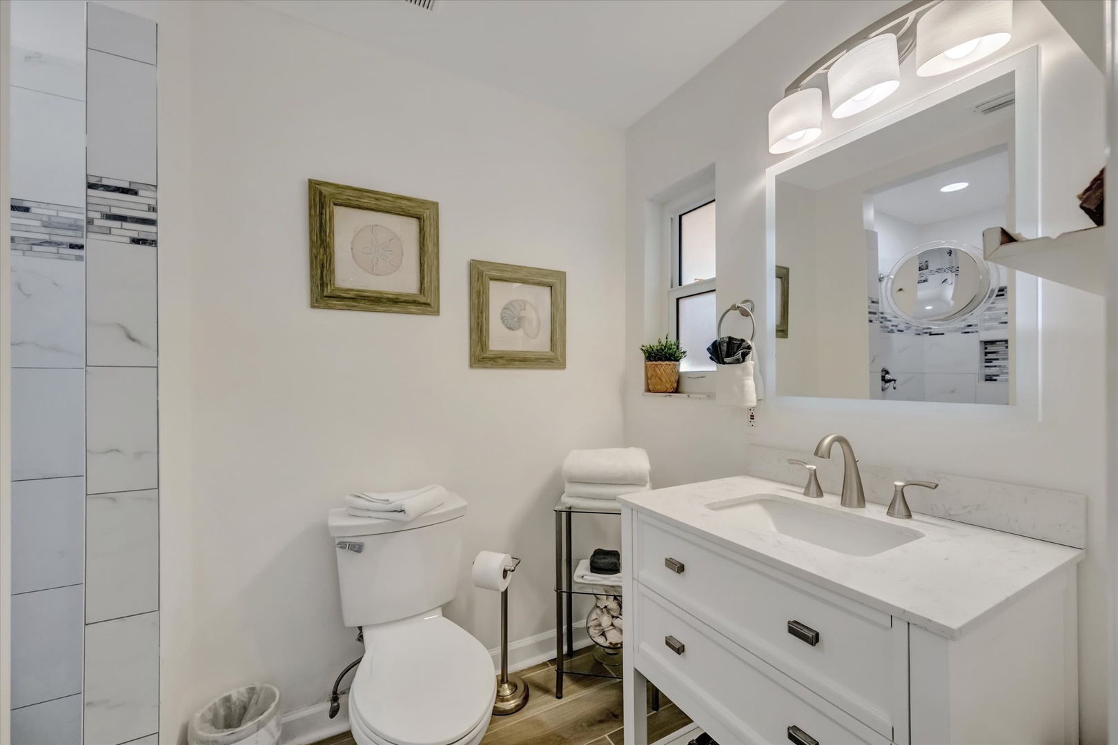Step into this bright, spotless bathroom where crisp white surfaces and warm wood accents create your personal retreat. Fresh towels await, and modern fixtures ensure your comfort.