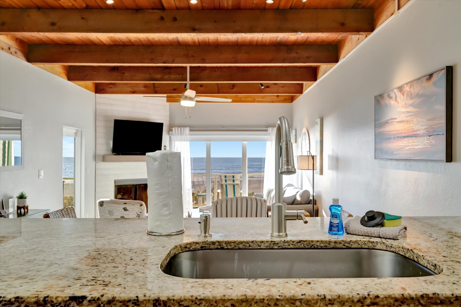From your kitchen, gaze out at the endless ocean stretching beyond the deck. Granite counters, warm wood beams overhead, and coastal light create a space where cooking feels effortless.