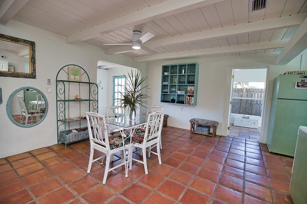 Step into a breezy coastal dining space where warm terracotta tiles meet whitewashed beams and soft breezes from the ceiling fan keep things cool. You'll love gathering here for meals surrounded by charming vintage touches.