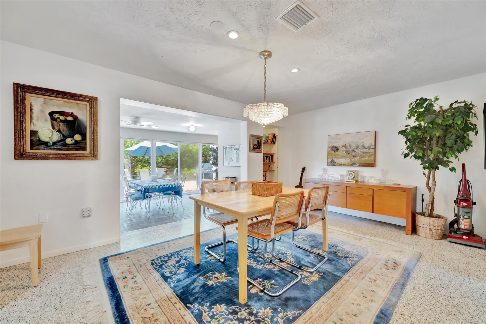 Gather around the inviting dining table where natural light pours in through glass doors, opening to your private outdoor terrace. The elegant chandelier and mid-century touches create a warm space for memorable meals together.