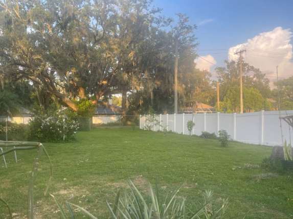 The property's fenced backyard offers plenty of open lawn space beneath mature shade trees, perfect for outdoor activities or simply relaxing in the peaceful residential setting.