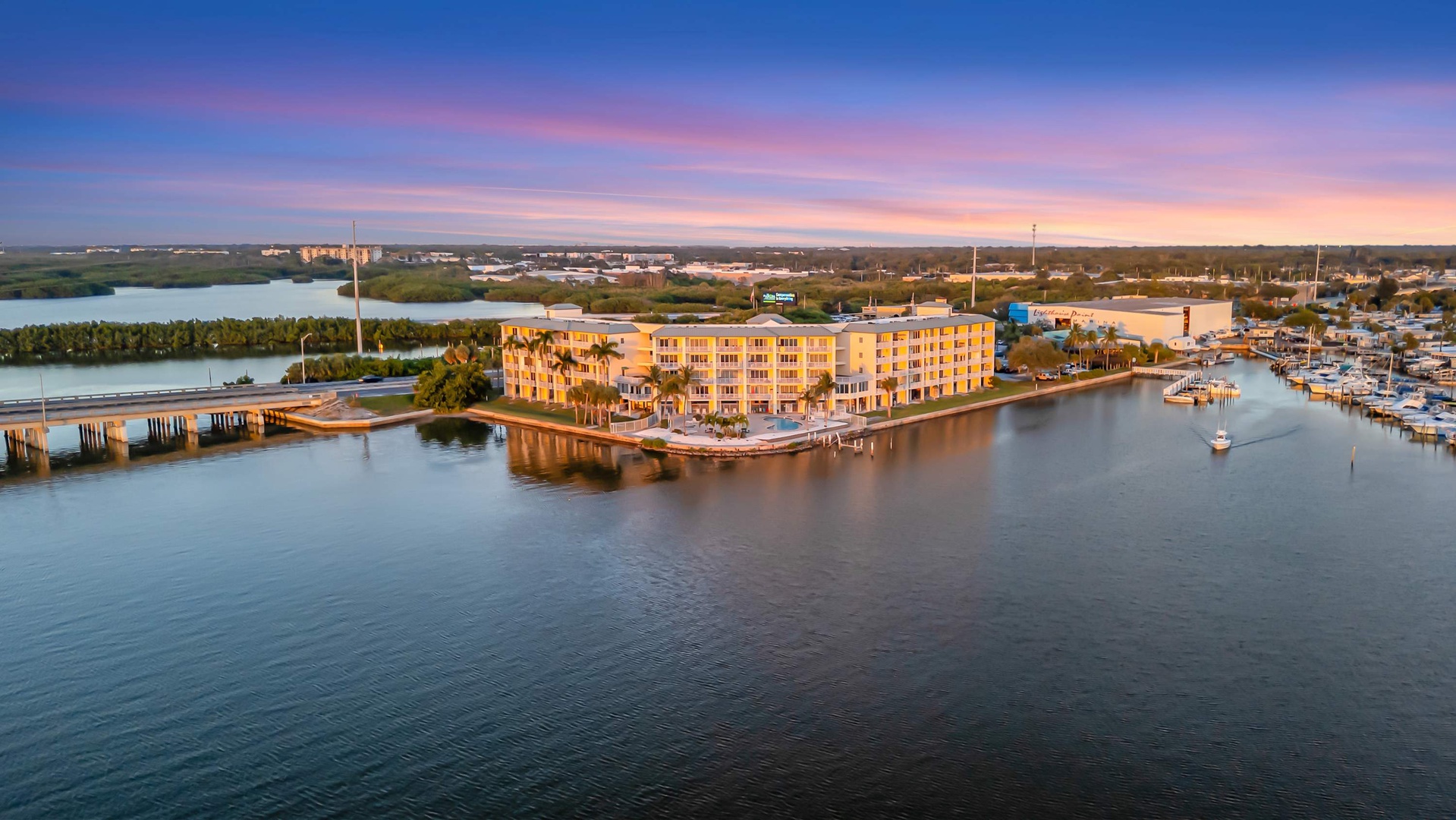 Waterfront property nestled on a scenic marina, surrounded by calm waters and distant natural landscapes, captured during a colorful sunset.