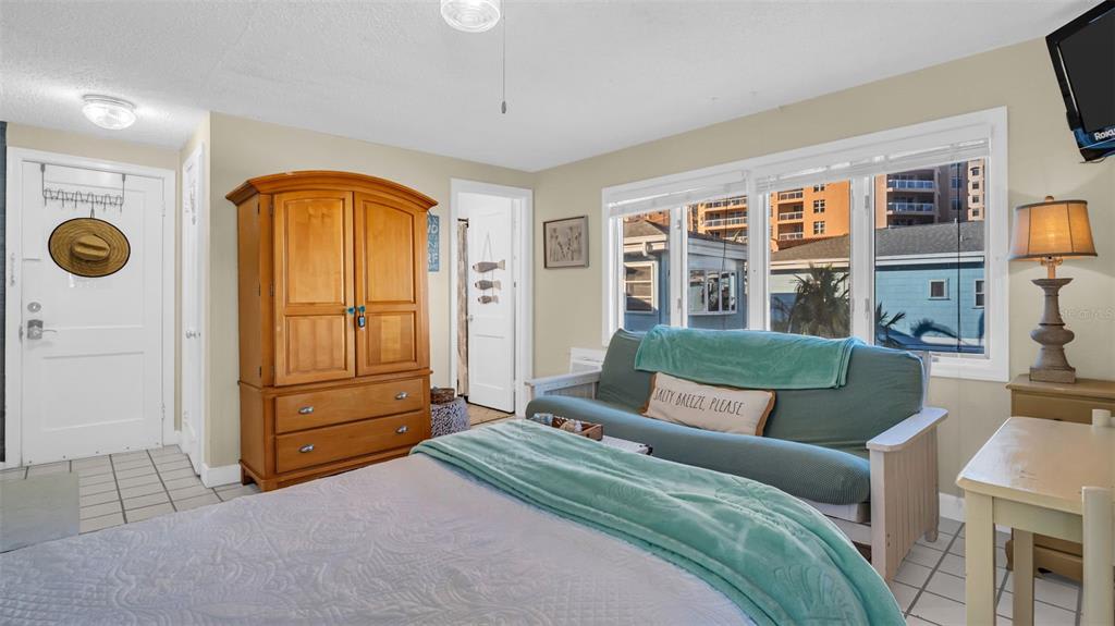 Relax in your beach-inspired bedroom with calming teal accents, warm wood furnishings, and city views through bright windows. Your peaceful coastal retreat awaits.