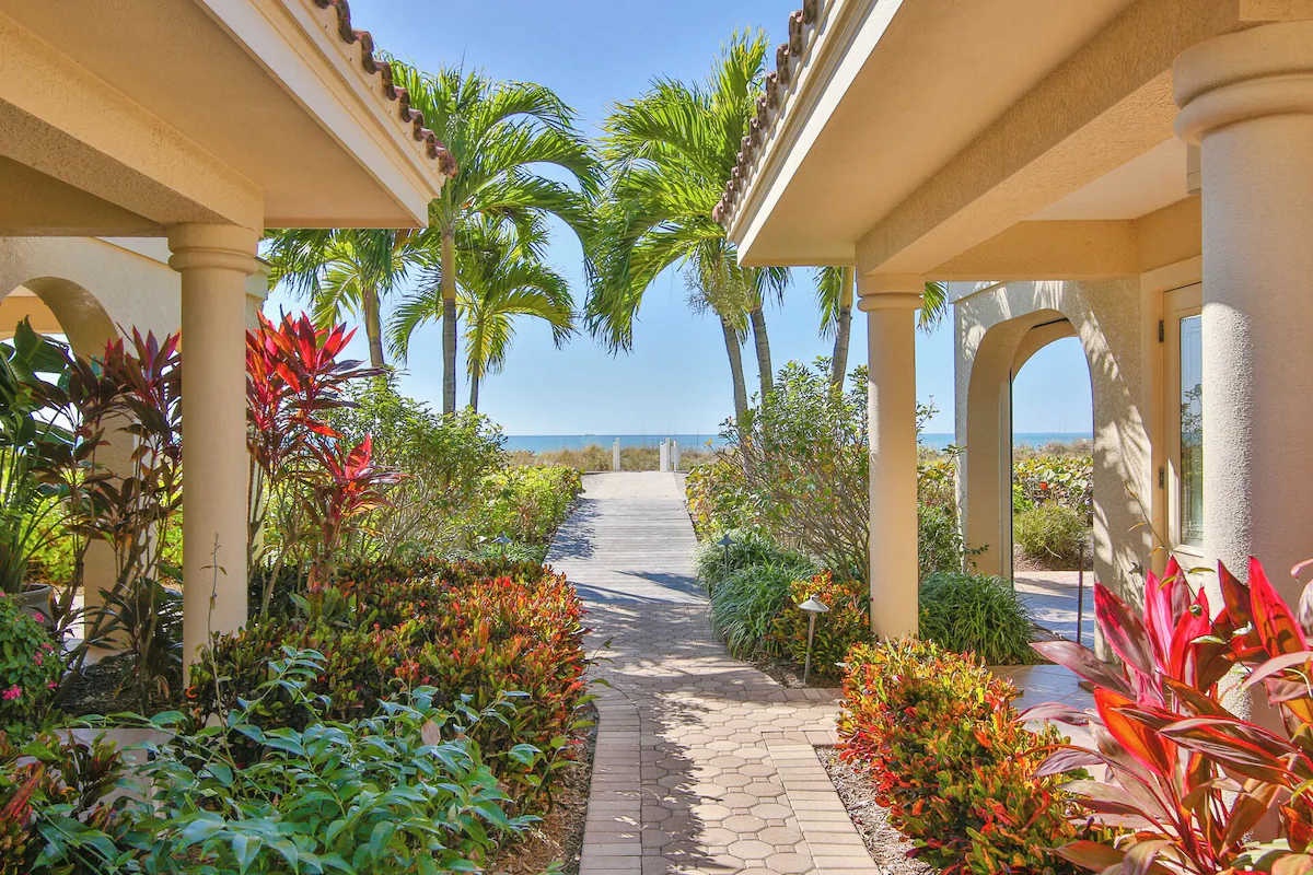 This elegant archway entrance opens onto a private pathway through vibrant tropical gardens, leading to stunning coastal scenery beyond.