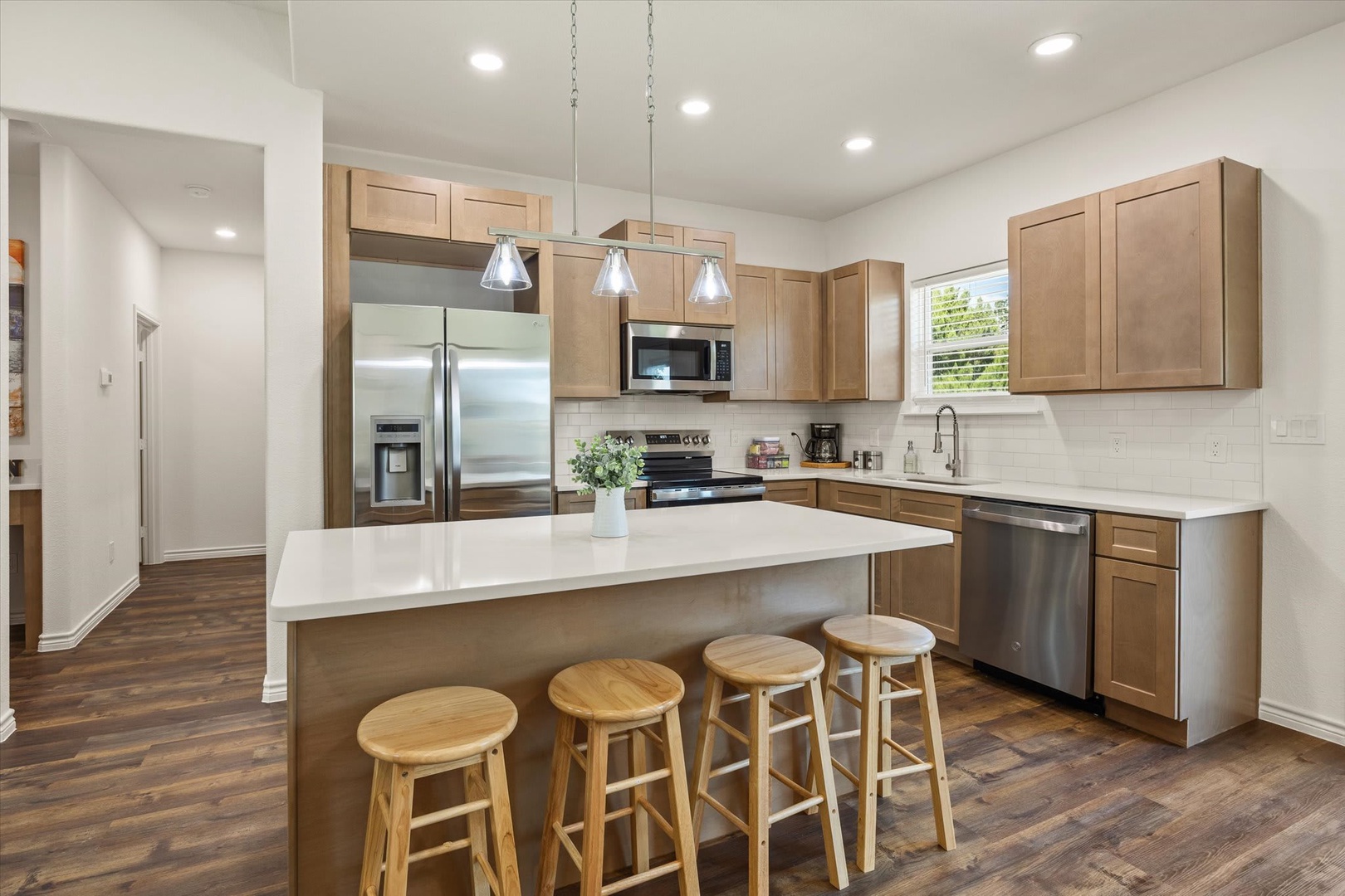 You'll love gathering around this spacious kitchen island with stainless appliances, warm wood cabinetry, and bright natural light streaming through the window above the sink.