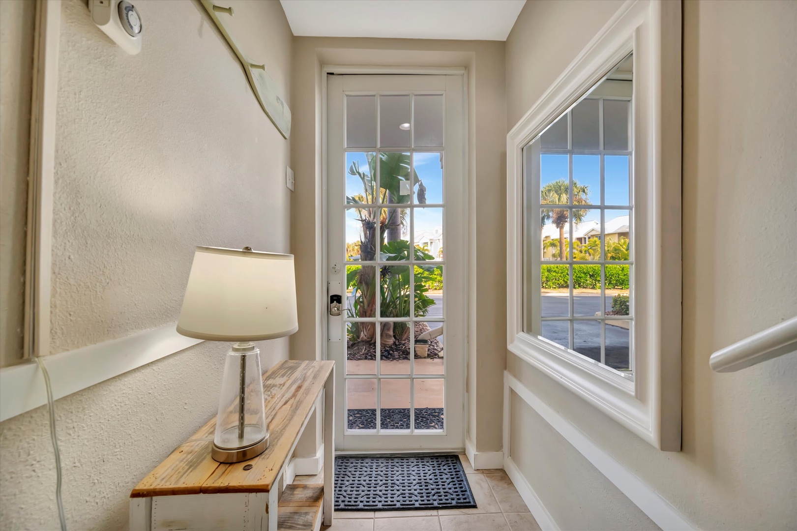 This bright, welcoming entryway frames a lush garden view through its glass door and window, setting the tone for your tropical escape. The warm lighting and thoughtful details create a calming, inviting first impression that feels like home.