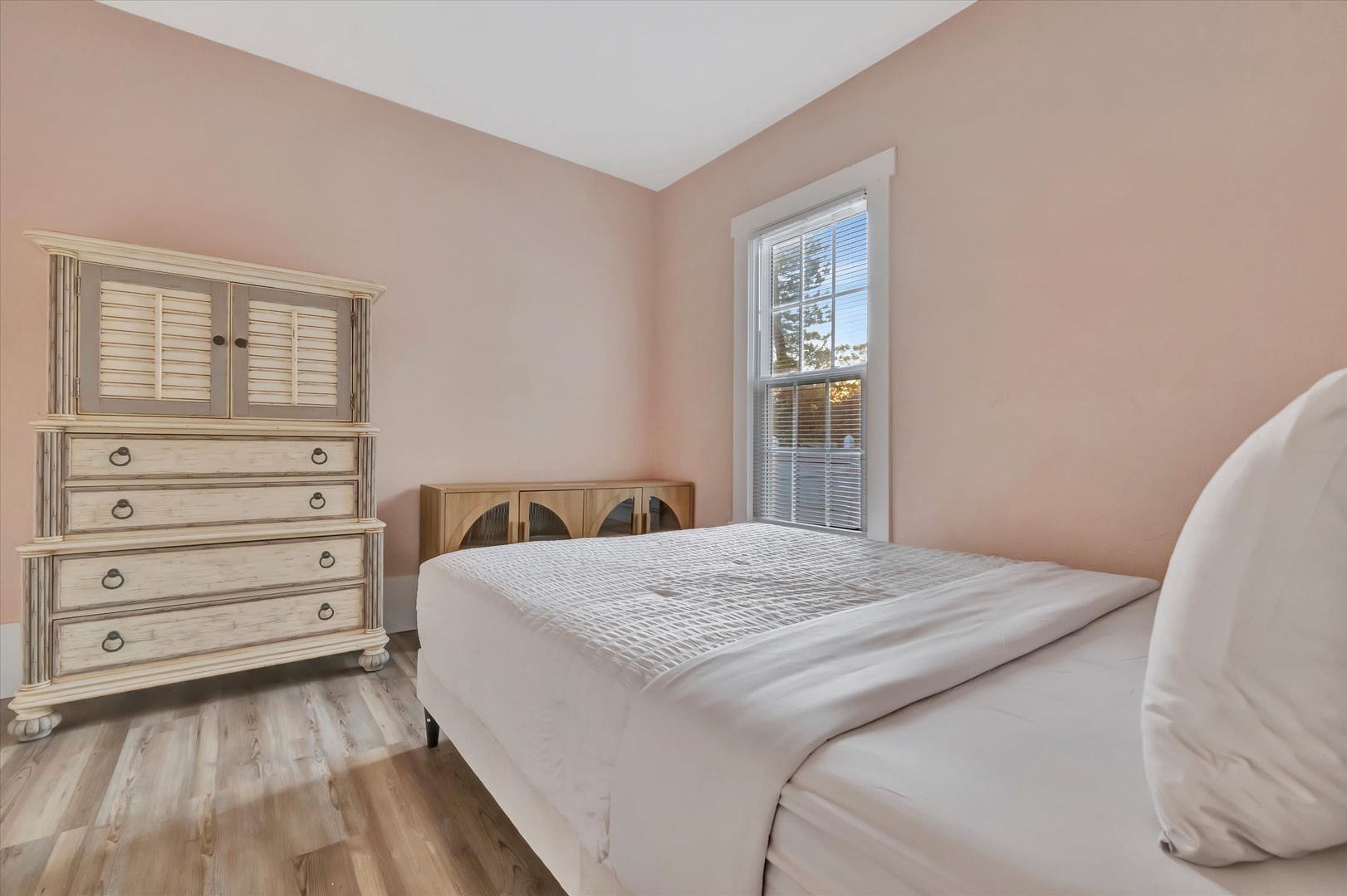 Settle into your peaceful bedroom with soft pink walls, natural light, and a cozy bed that invites restful nights. The warm wood floors and elegant dresser add charm to your private retreat.