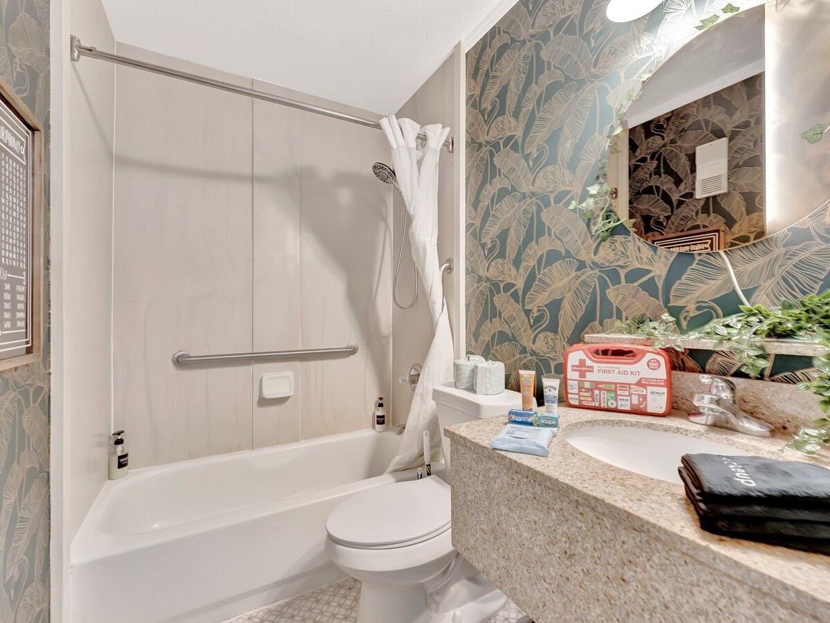 Your private bathroom features a tub-shower combo with safety rails, a fresh tropical-inspired accent wall, and all the essentials for a comfortable stay.