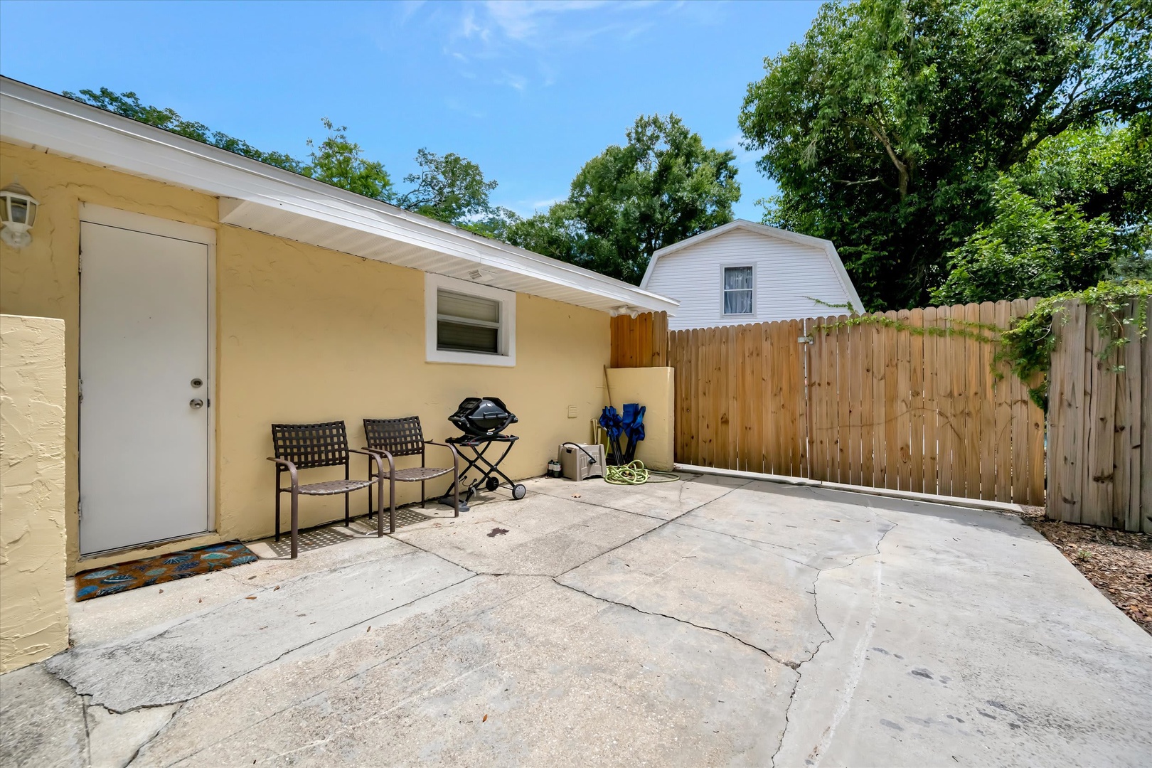 Your private outdoor patio awaits with seating and a grill for easy meals under the open sky, nestled in a peaceful, tree-lined yard.