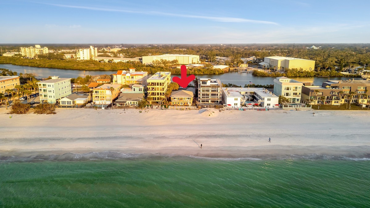 An aerial view of beachfront properties along a pristine stretch of sand and turquoise waters, with the marked building offering direct beach access in a scenic coastal community.