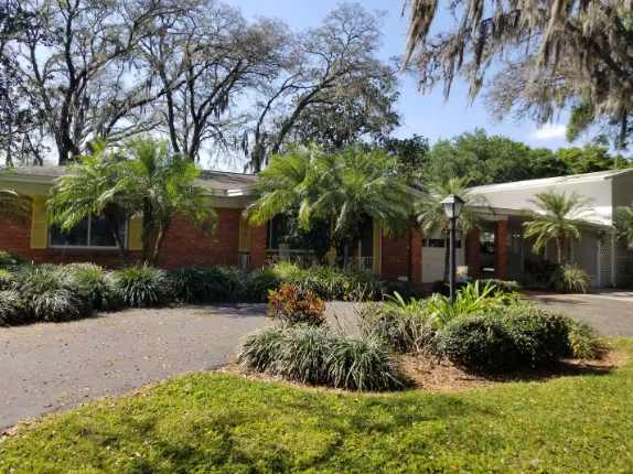 This charming mid-century property is surrounded by lush tropical landscaping and mature oak trees draped with Spanish moss, creating a peaceful retreat atmosphere.