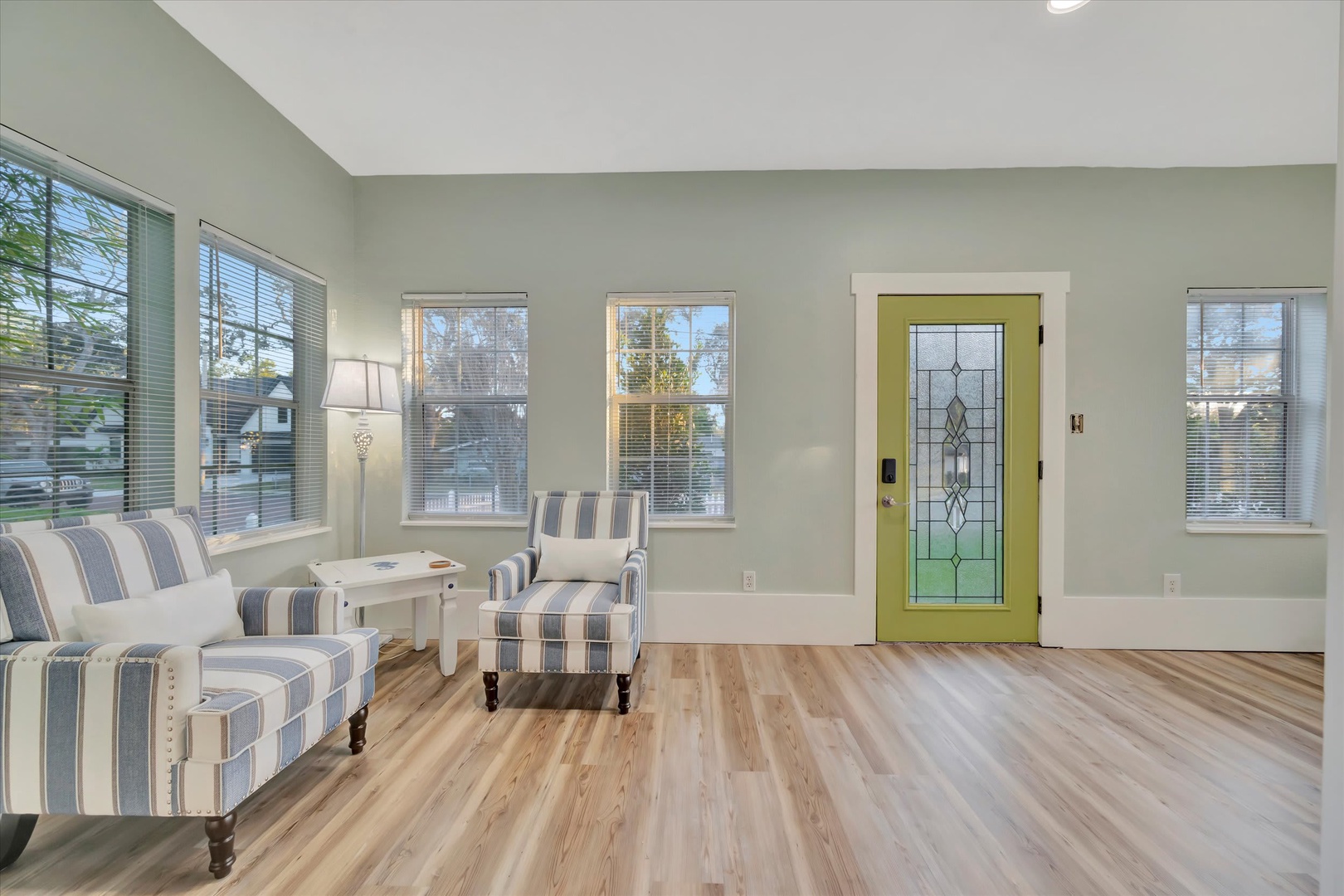 Settle into your bright, airy living space where natural light pours through oversized windows and a charming green door welcomes you home. The soft coastal tones and comfortable seating create the perfect spot to unwind after a day exploring.