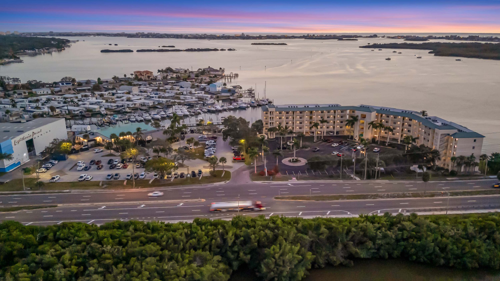 Aerial view of the property positioned along scenic waterfront surroundings at dusk, with convenient access and nearby amenities visible in the neighborhood.