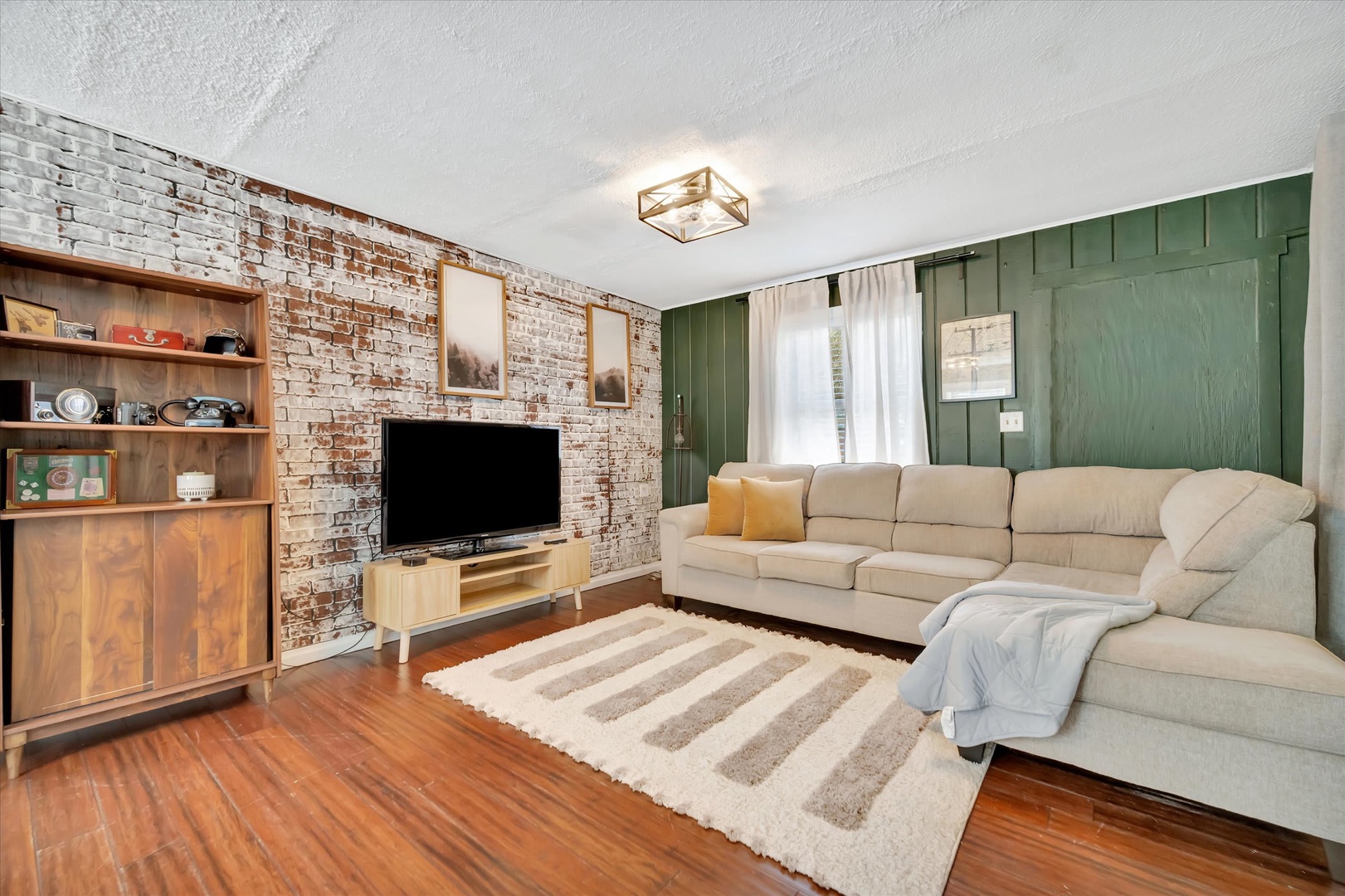 Sink into the plush sectional and relax in this inviting living room, where exposed brick meets modern green accents and warm wood floors create a perfect blend of character and comfort.