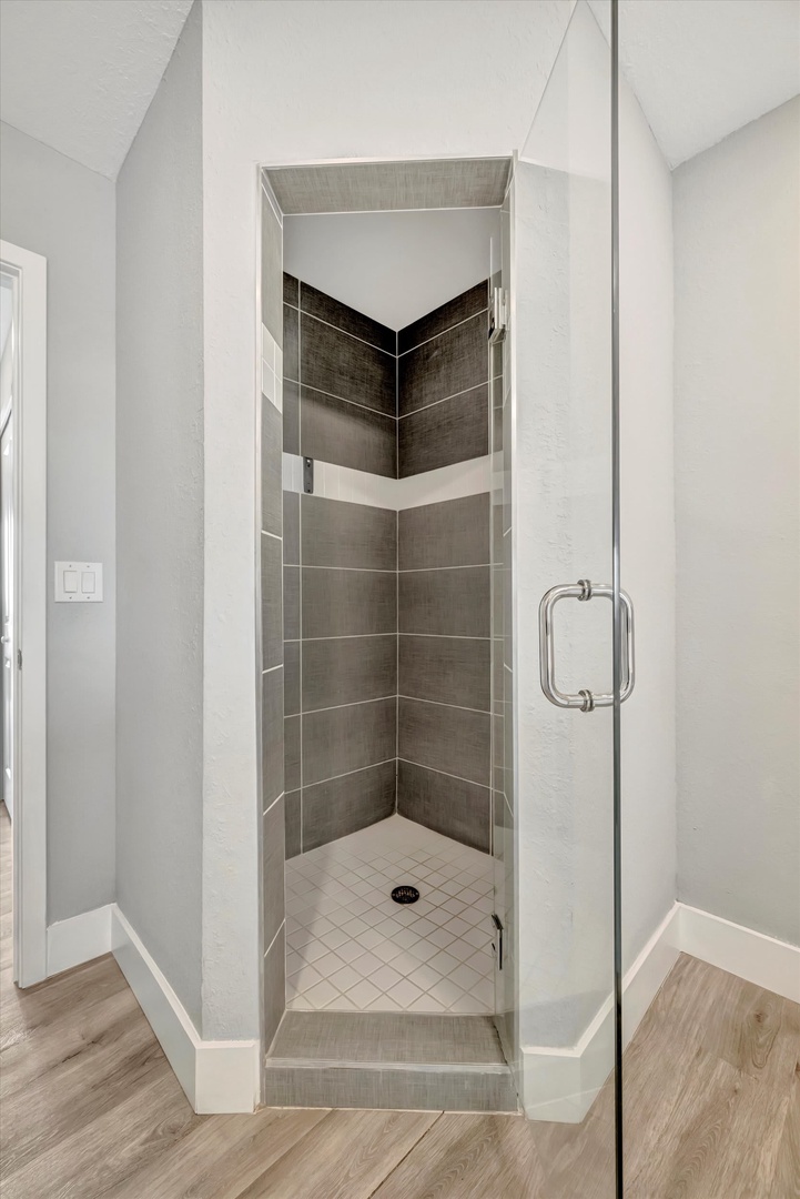 Step into your private glass-enclosed shower, where sleek gray and black tiling creates a spa-like retreat. The soaring vaulted ceiling adds unexpected luxury to your daily routine.