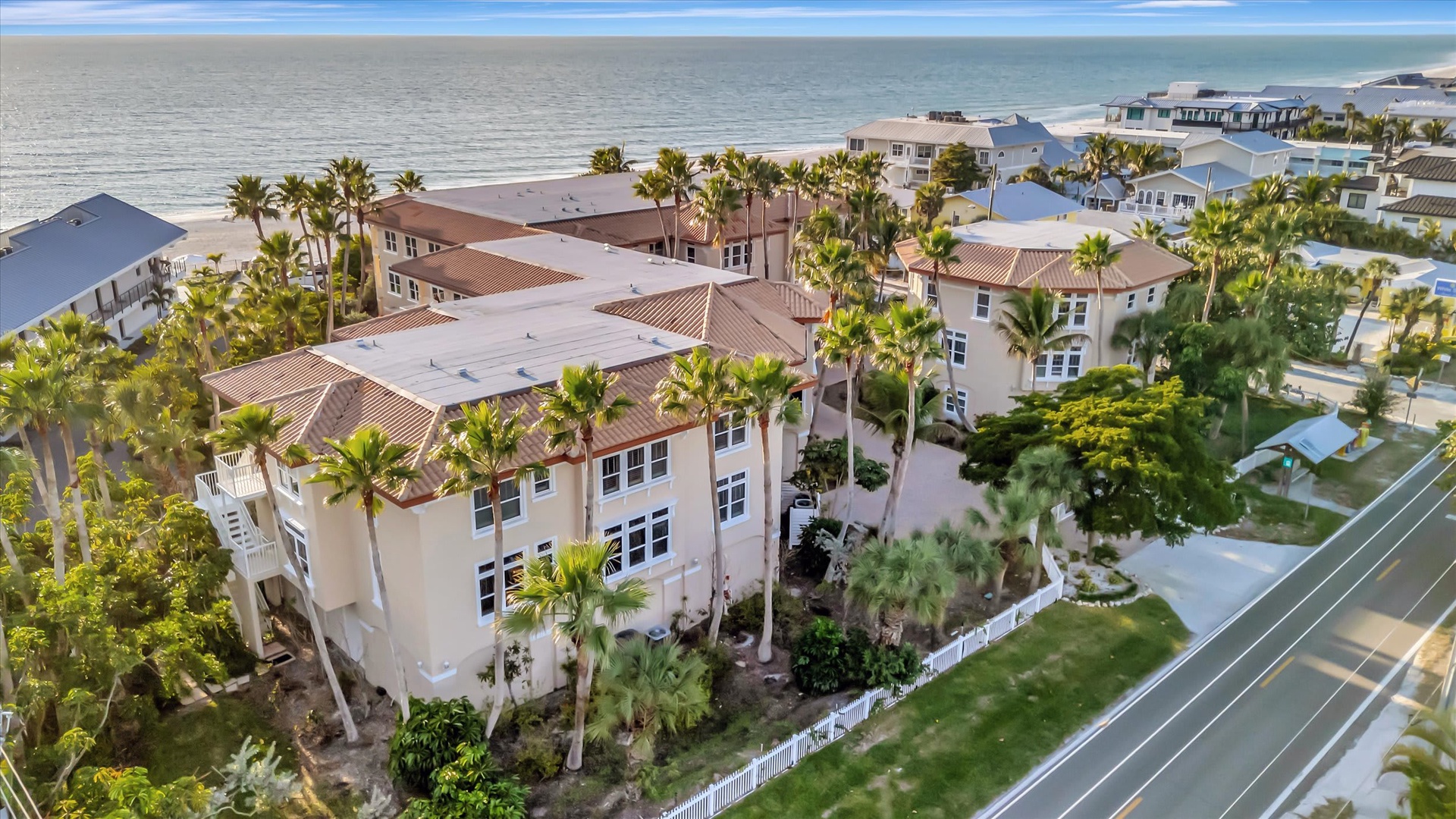 Aerial view of a beachfront vacation property nestled among palm trees with direct access to sandy shores and coastal neighborhood charm.