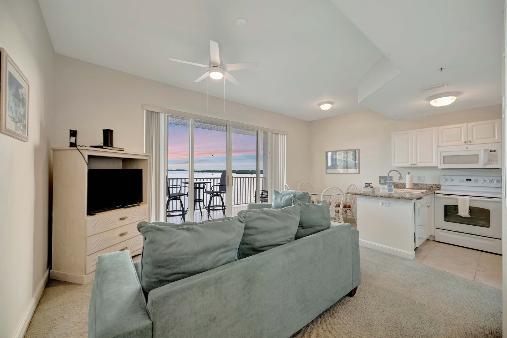 Settle into this comfortable living space where soft evening light filters through balcony doors, creating the perfect setting to unwind. The open layout connects the kitchen and dining areas for easy meal preparation and quality time together.