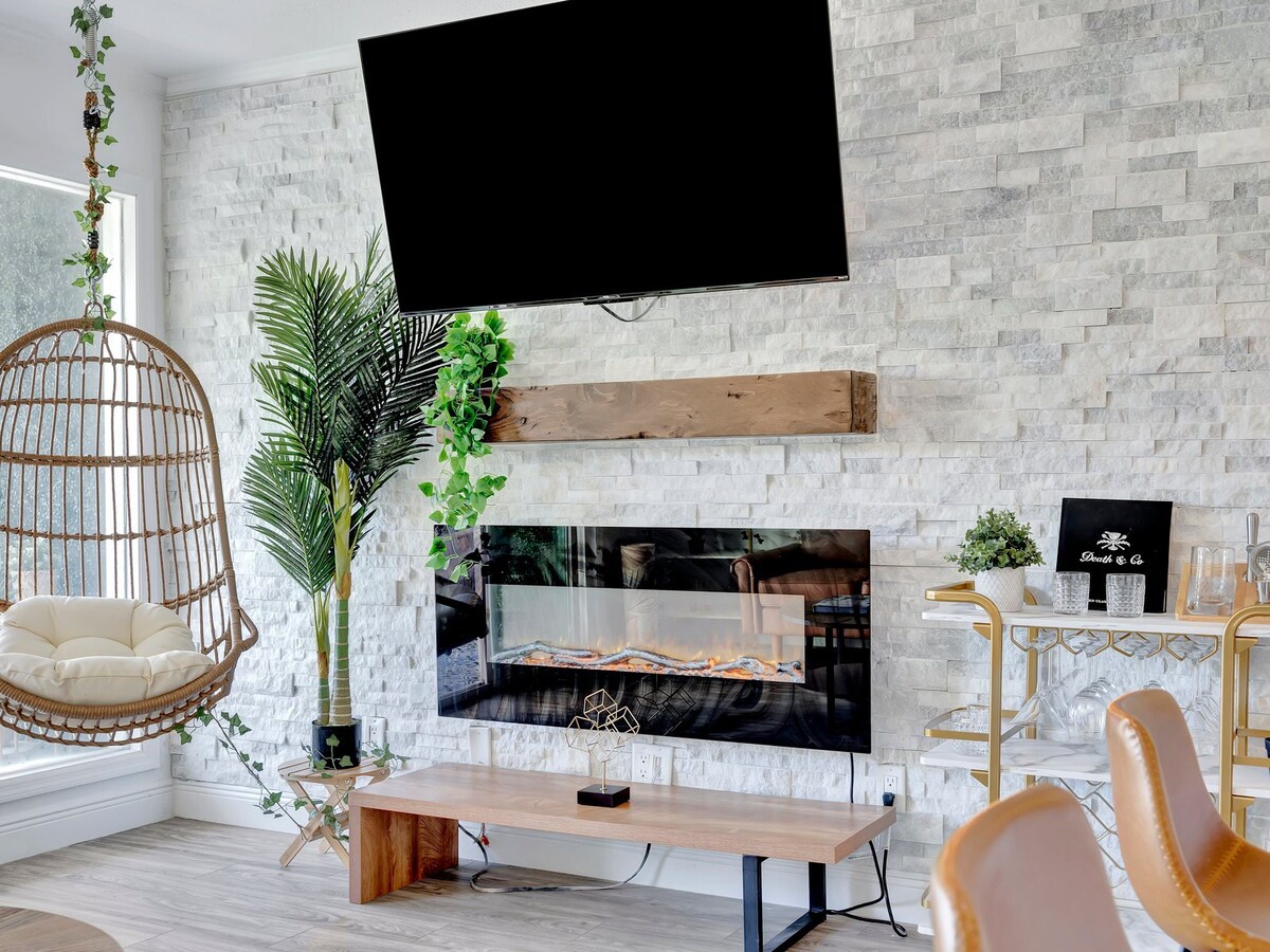 Settle into your stylish retreat where modern meets cozy—a chic hanging chair, warm fireplace, and fresh greenery create your perfect relaxation corner.