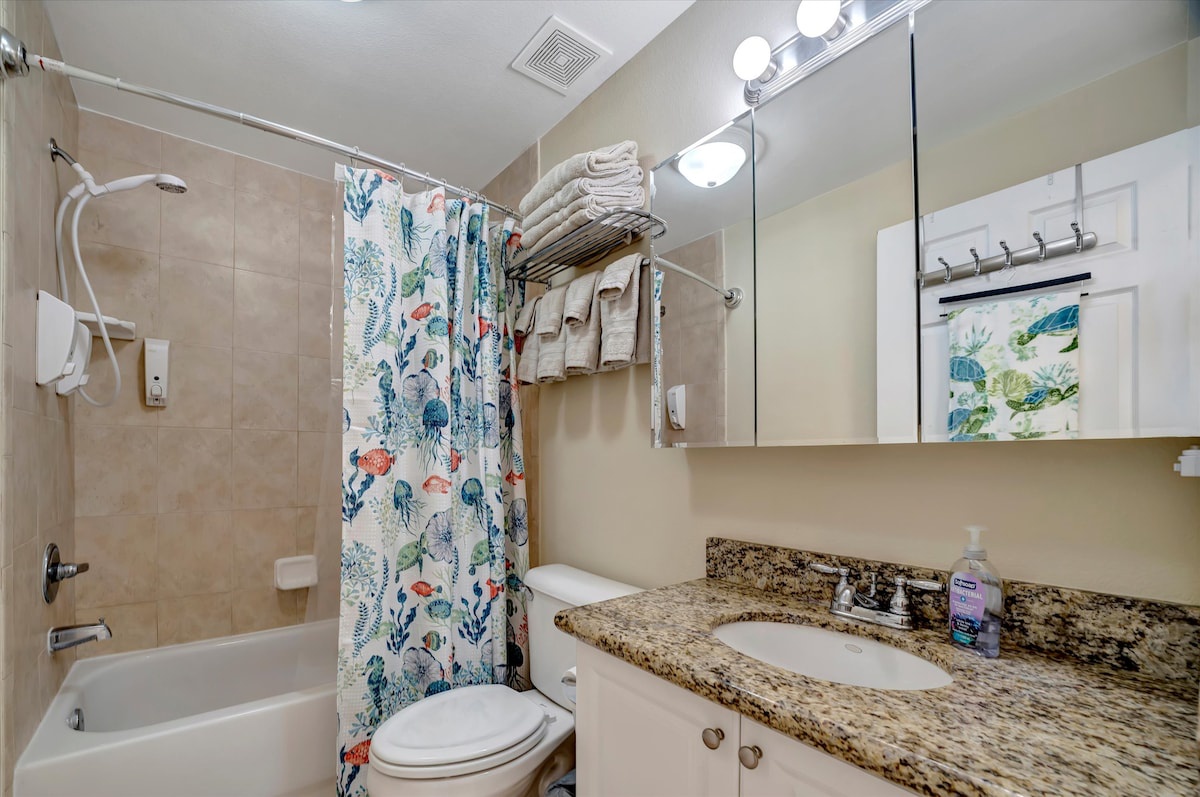 Step into your bright, spotless bathroom where fresh towels await and a cheerful coastal-themed shower curtain adds a splash of color to your relaxing retreat.