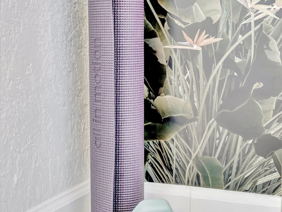 A rolled yoga mat rests against a botanical accent wall, ready for your morning stretch or evening wind-down in this serene space.