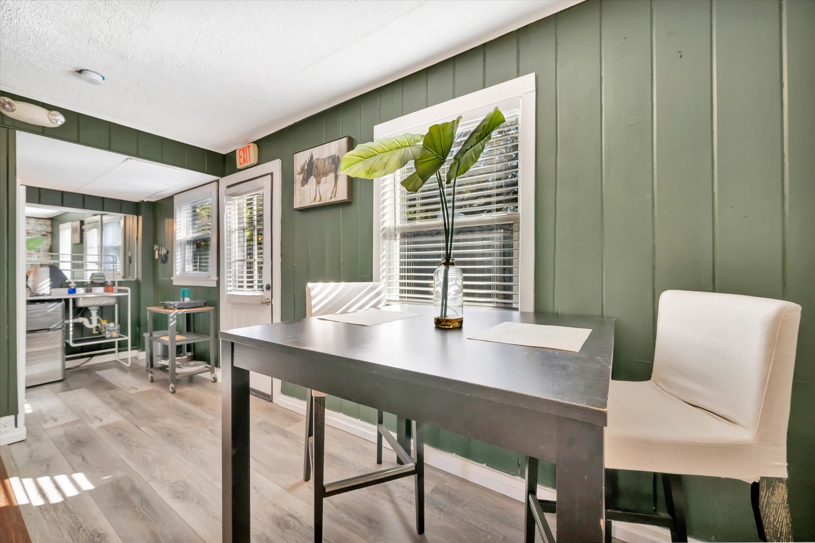 Step into your stylish workspace with rich sage-green paneled walls and natural light streaming through plantation shutters. The modern desk and seating create the perfect spot to catch up on emails or plan your day's adventures.