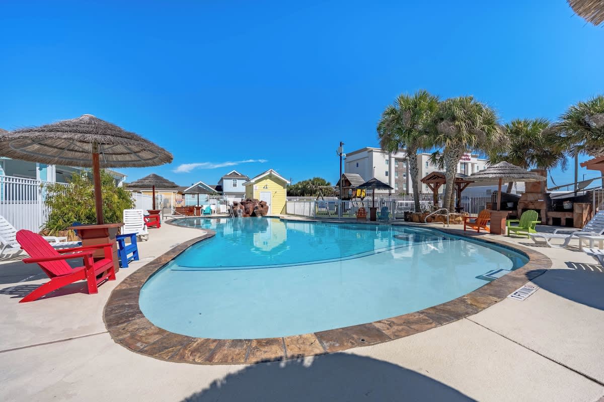 Soak up the sun by the sparkling pool, surrounded by colorful Adirondack chairs and shaded by thatched umbrellas—your perfect spot to unwind with the coastal breeze and tropical palm trees overhead.