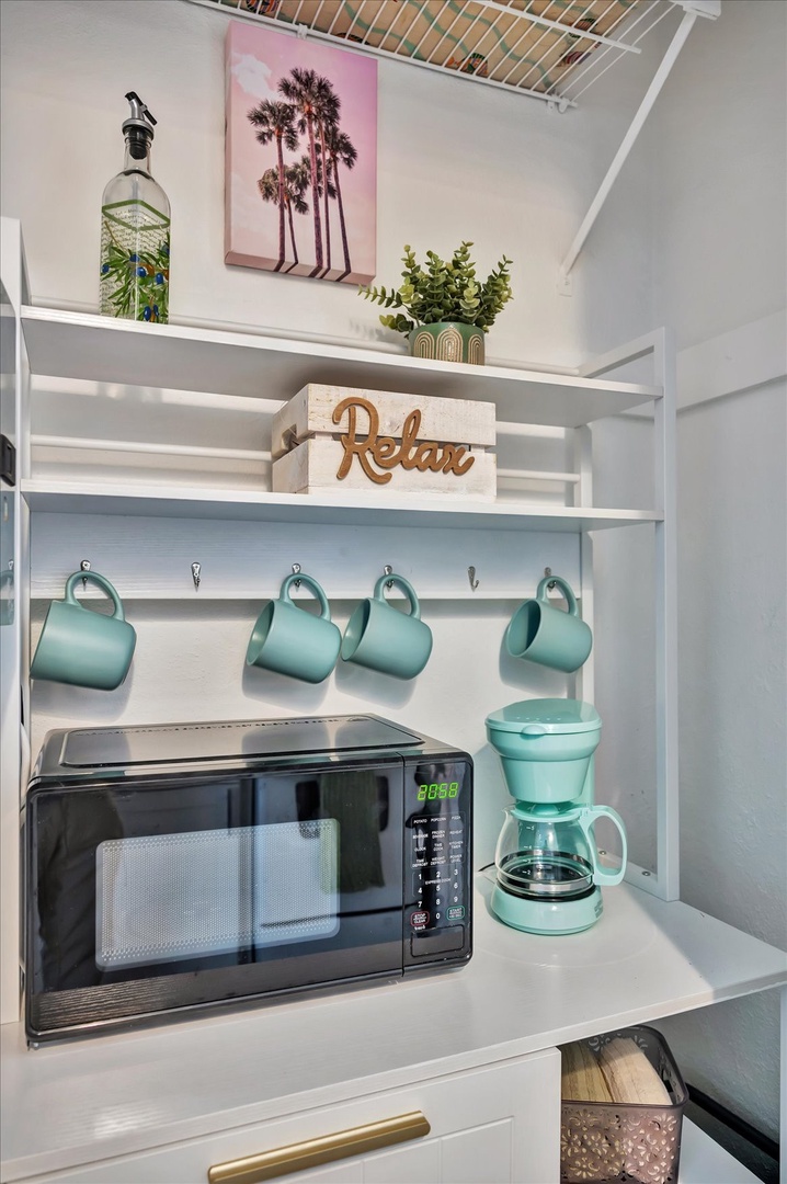 Your mini kitchen nook has everything you need to start the day right—fresh coffee, a microwave for quick meals, and cheerful turquoise mugs hanging ready for use.