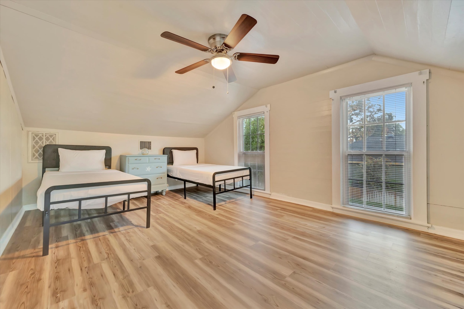 Stretch out in your spacious upstairs bedroom, where vaulted ceilings and a ceiling fan keep things comfortable. Natural light fills the room through large windows, and the warm hardwood floors add a welcoming touch.