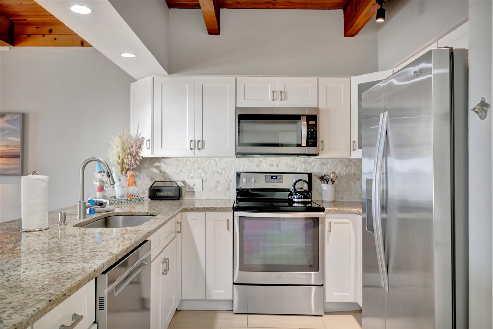 Your fully equipped kitchen features gleaming stainless appliances, granite counters, and warm wood beams overhead—ready for morning coffee or preparing a feast after exploring the area.