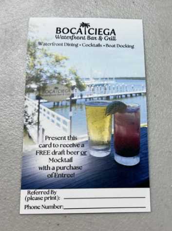 A promotional card for Boca Ciega Waterfront Bar & Grill sits on a textured surface, advertising a free draft beer or mocktail with entree purchase—perfect for planning your next dining adventure.