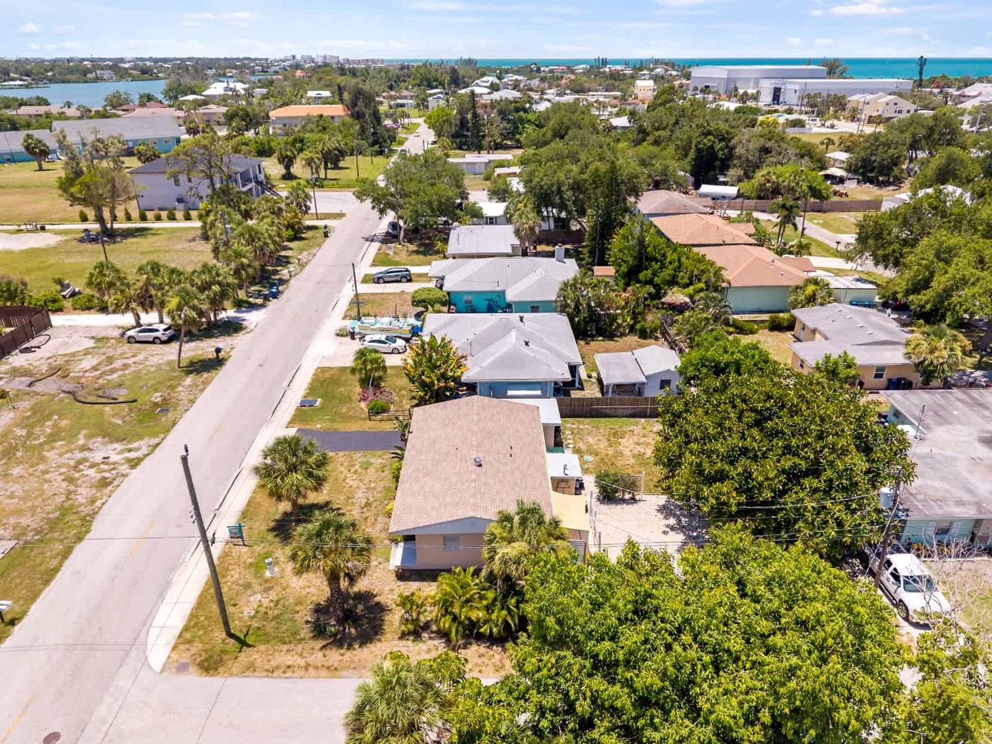 Aerial view showing the property nestled in a quiet residential neighborhood, with palm trees and coastal waters visible in the distance.