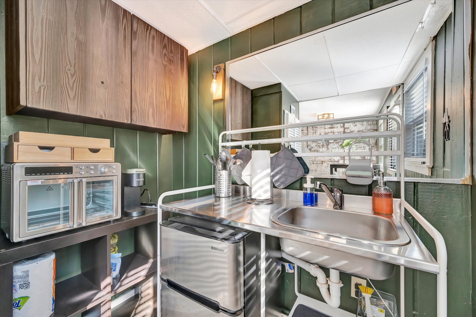 Your compact kitchenette has everything you need—microwave, mini-fridge, sink, and storage—all thoughtfully arranged in a cozy space with charming green paneled walls.