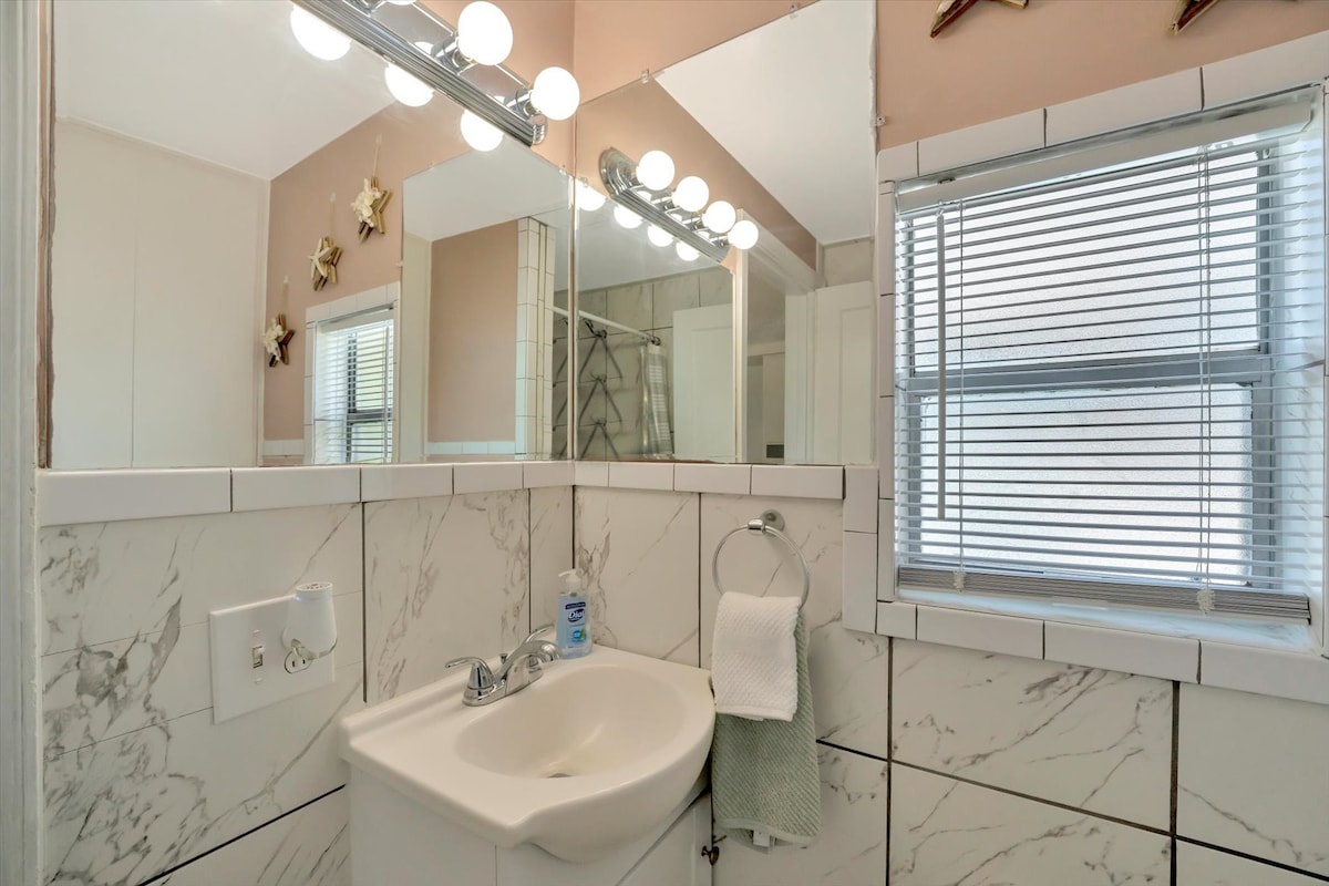Slip into this bright, marble-tiled bathroom where vanity lighting and a large mirror make your morning routine effortless. Fresh towels await, and natural light filters gently through the blinds.