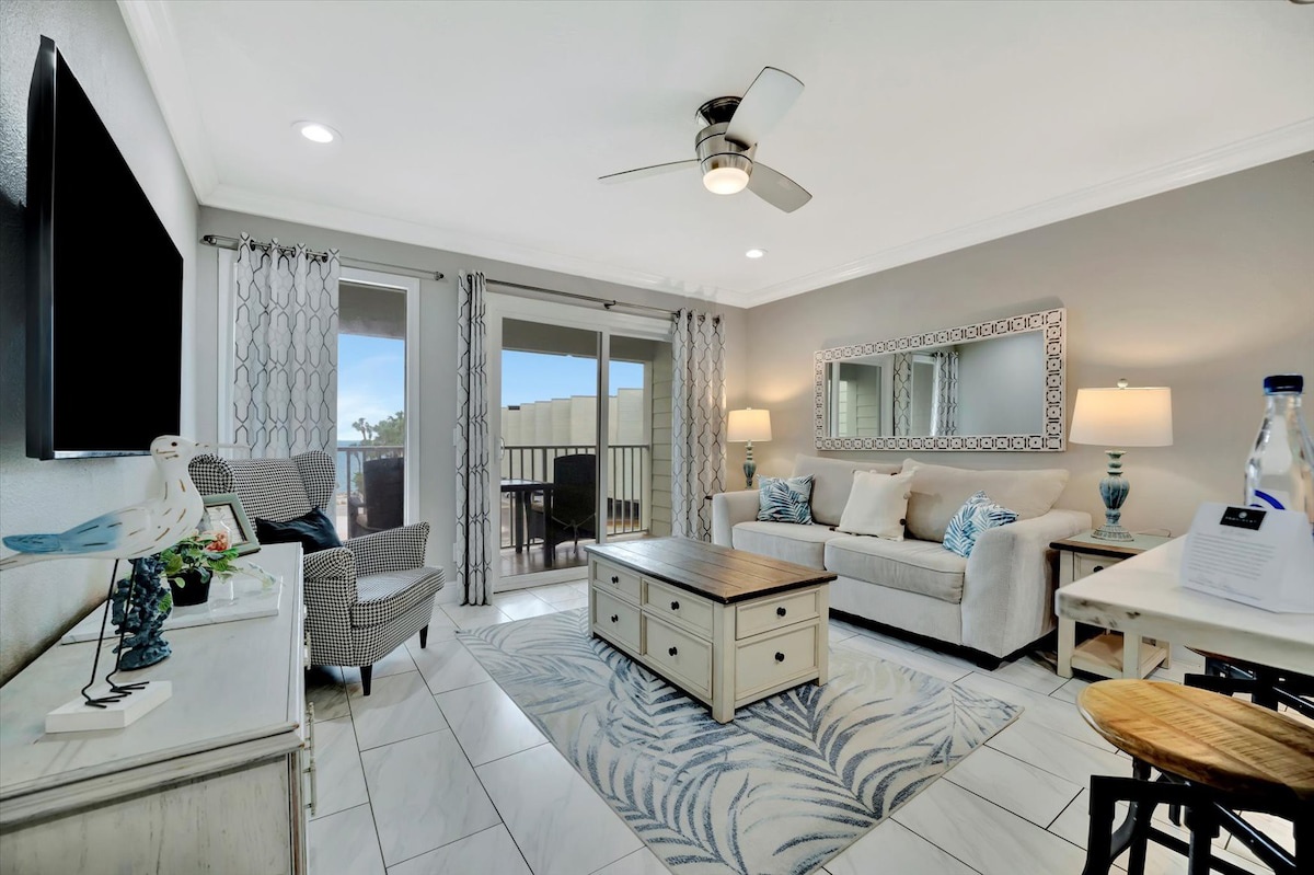 Unwind in your light-filled living room where coastal elegance meets comfort—sink into the plush sofa, enjoy the ceiling fan's gentle breeze, and step out to your balcony for fresh air.