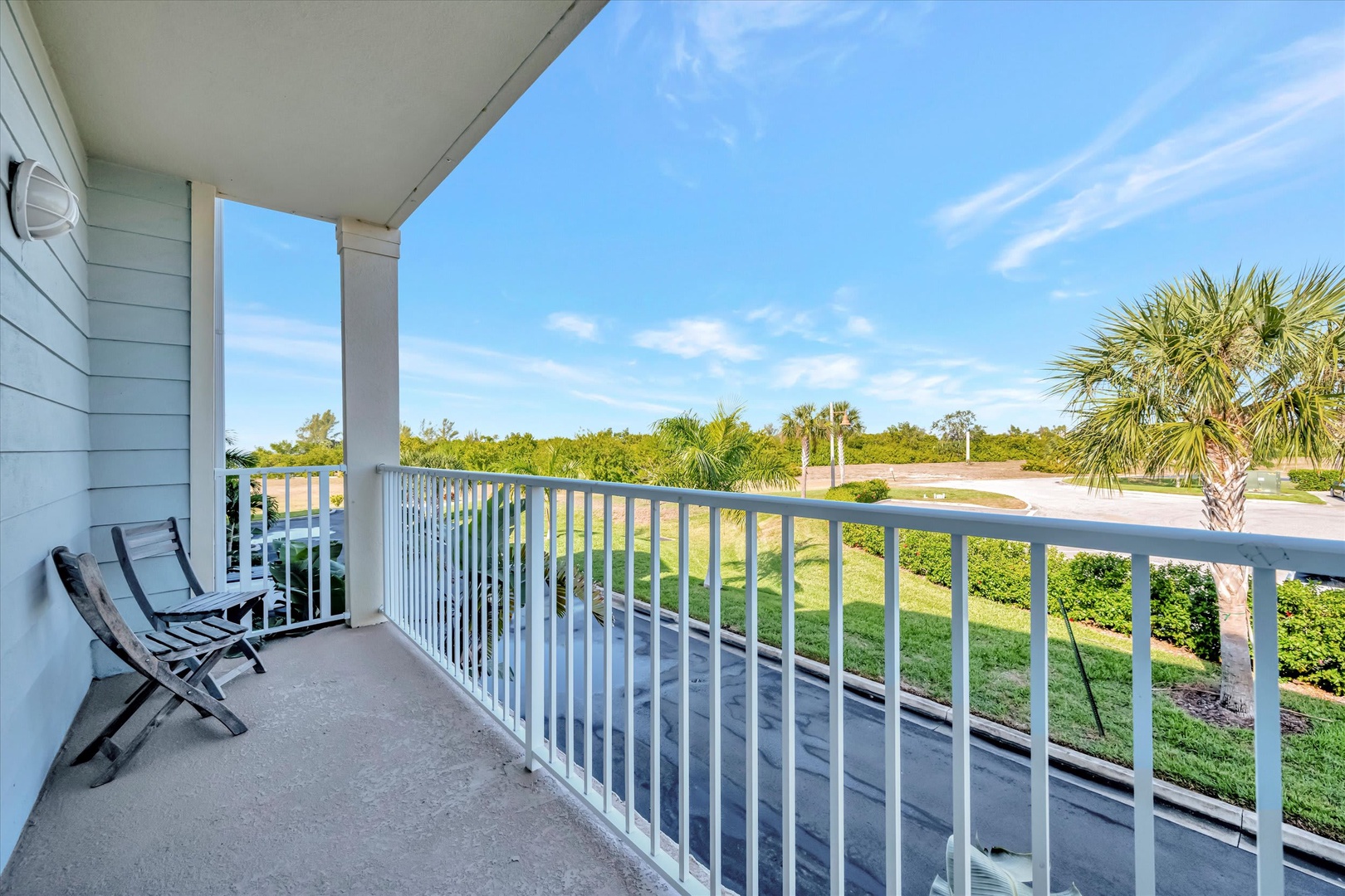 A covered balcony with folding chairs overlooks the property's lush green lawn and tropical palm trees, offering a peaceful spot to enjoy the Florida sunshine and fresh air.