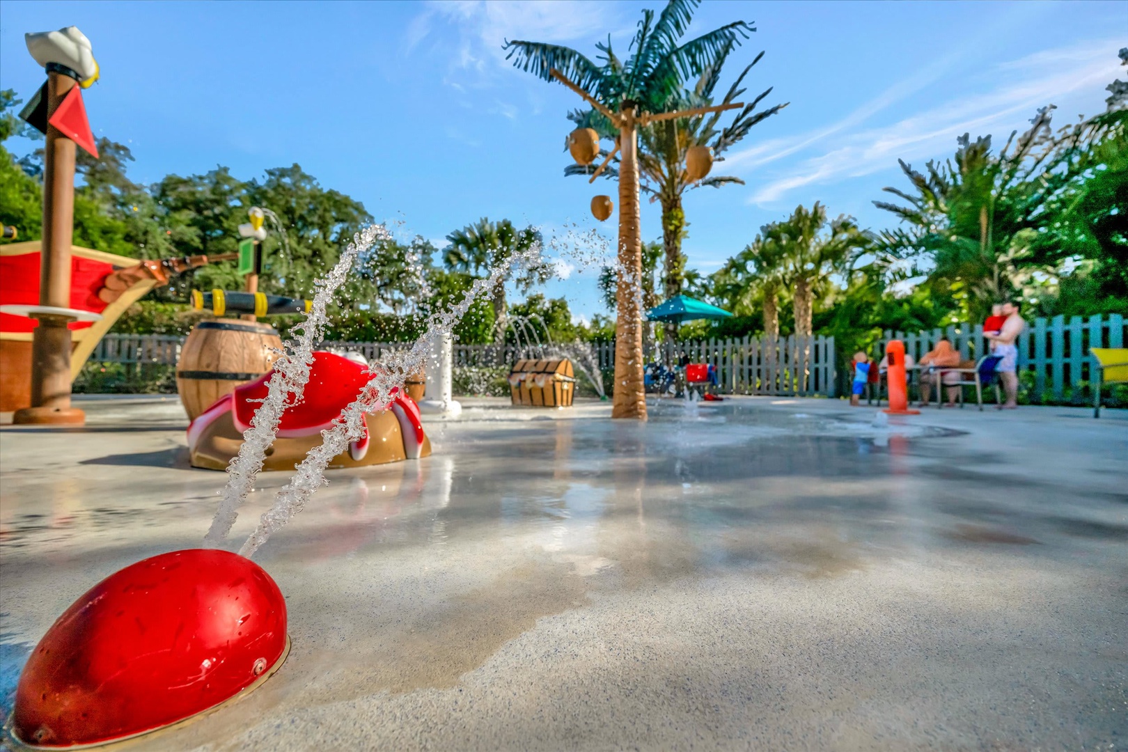 A vibrant splash pad with playful fountains and tropical palm trees creates the perfect space for family fun under sunny skies.