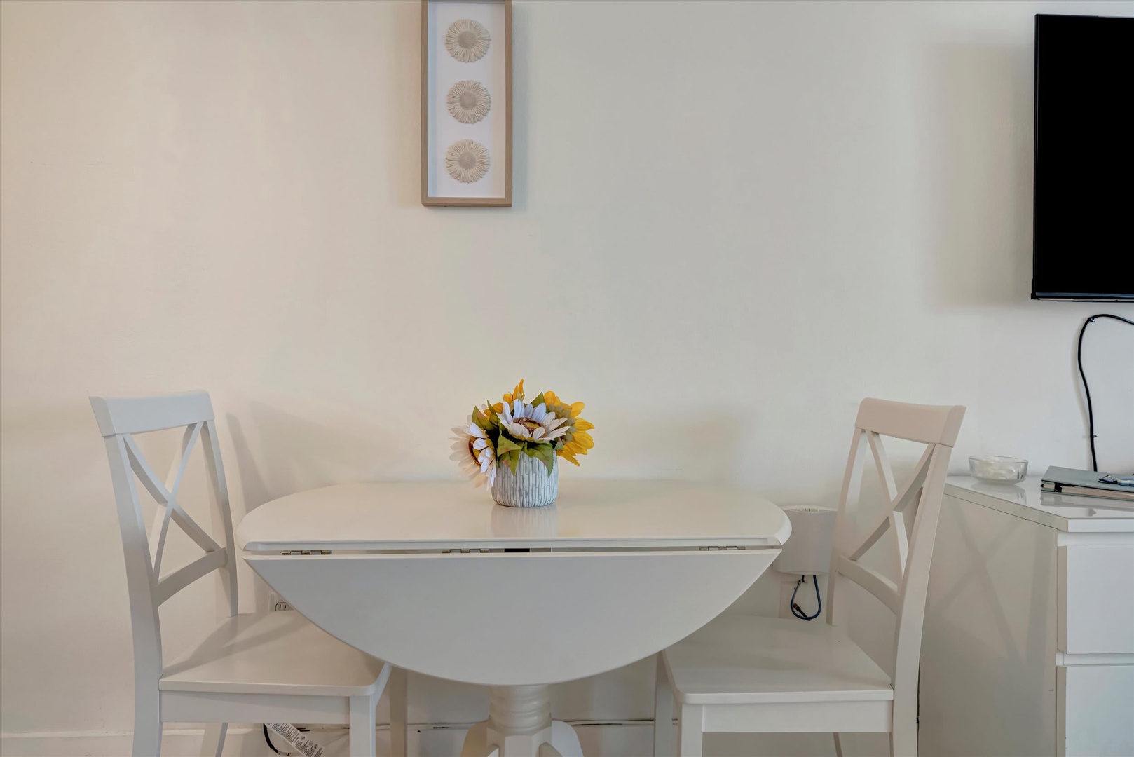 Enjoy your morning coffee at this charming bistro table, perfectly sized for two and brightened by a cheerful sunflower arrangement. Light and airy, it's your spot for planning the day ahead.