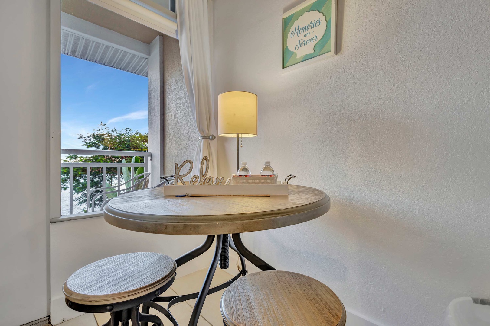 Step into your cozy breakfast nook with a charming bistro table, perfect for morning coffee or catching up on vacation plans. Natural light streams through the open balcony door, inviting gentle breezes and glimpses of greenery outside.