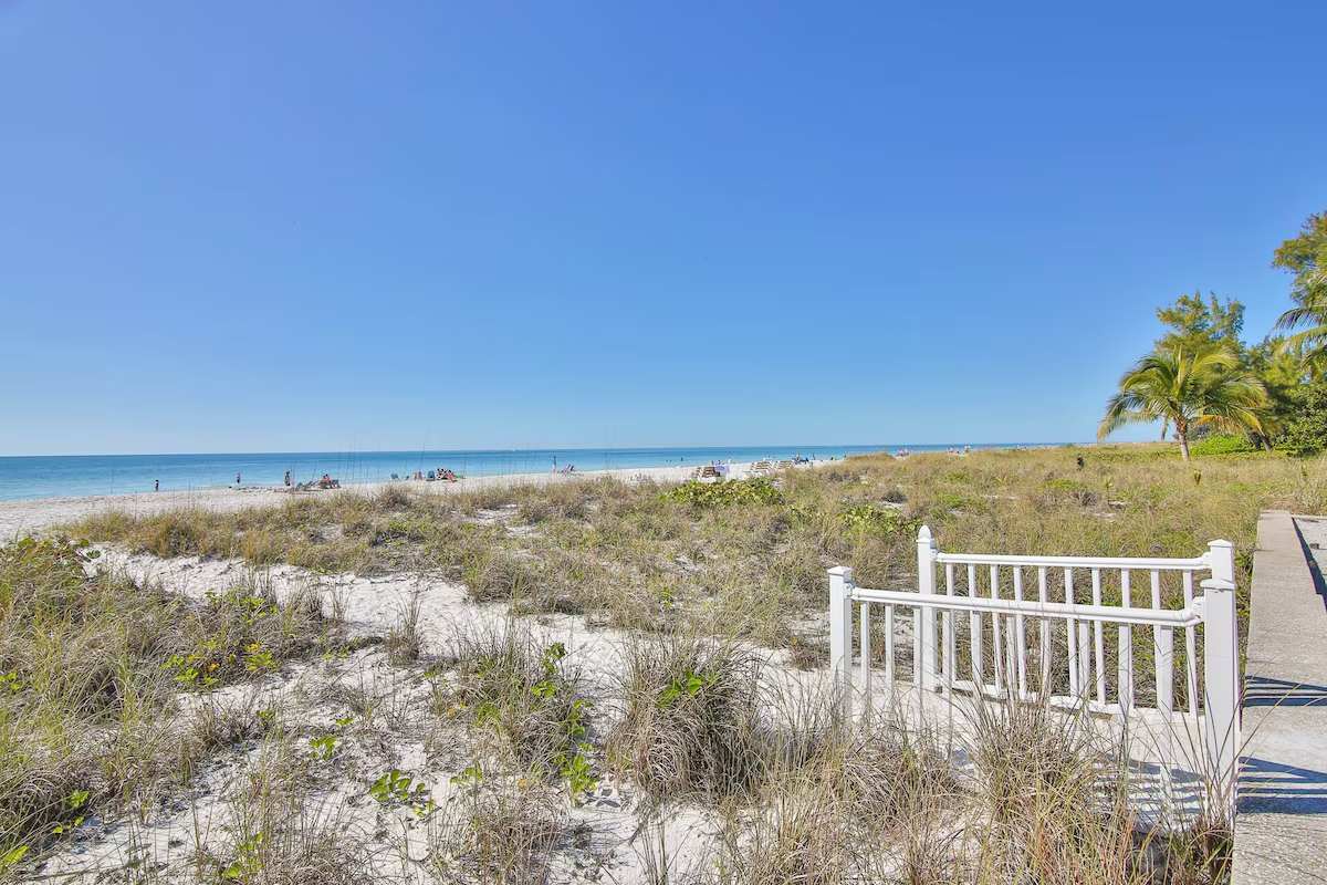 A private walkway leads through natural dunes to a pristine stretch of sandy shoreline, framed by swaying palms and endless turquoise waters—your perfect beach escape awaits.