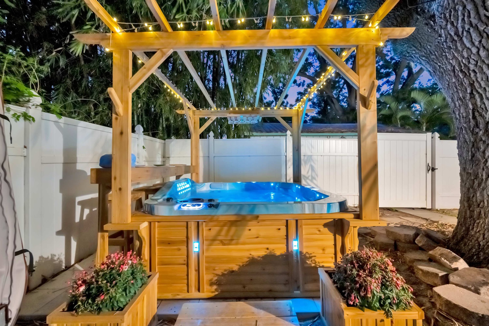 Unwind under twinkling string lights in your private hot tub, surrounded by lush greenery and a beautifully crafted pergola—your perfect evening retreat.