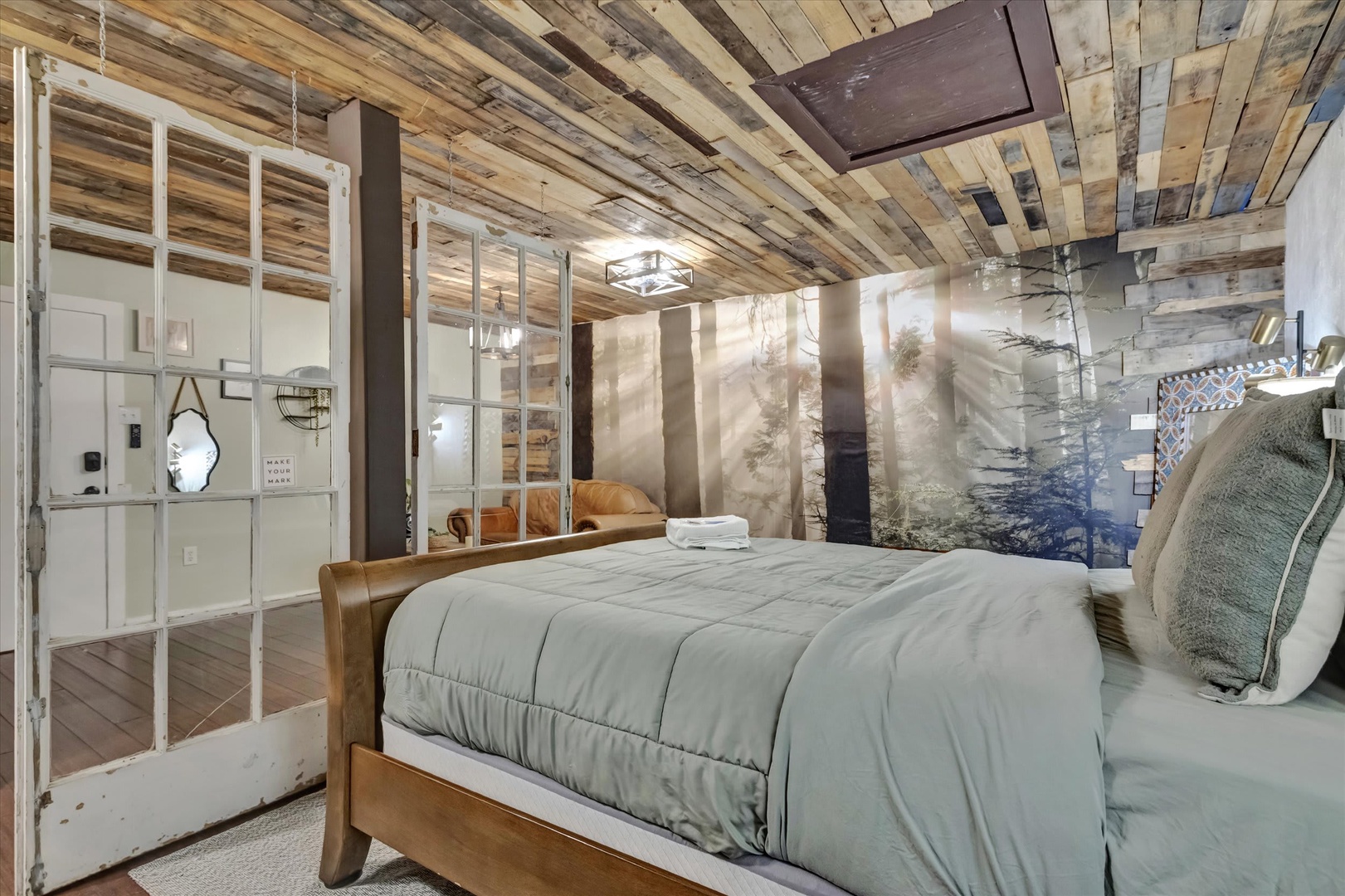 Drift off beneath a stunning reclaimed wood ceiling, where natural light filters through soft curtains to create a serene, artfully crafted retreat. Your cozy bed awaits with plush linens and rustic warmth.