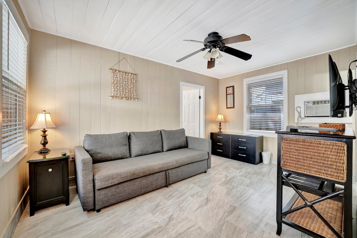 Settle into your bright, airy living space with fresh coastal vibes. The plush sofa invites you to kick back under gentle ceiling fan breezes, while warm lamps and natural light create the perfect spot for relaxing.