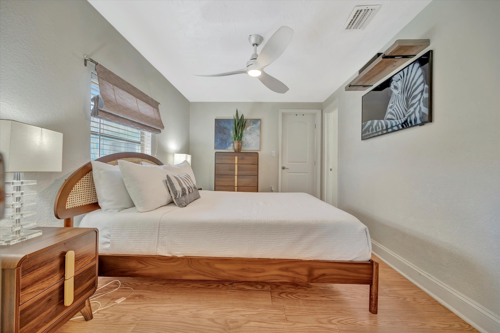 Sink into crisp linens and let the gentle ceiling fan breeze lull you to rest in your serene coastal-inspired bedroom with warm wood accents and soothing neutral tones.
